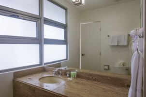 Un baño con un ventanal grande, un lavamanos, un espejo y un perchero para toallas.