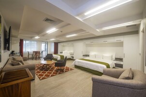 Una habitación de hotel moderna con sofá, dos camas, una mesa de comedor y televisor.