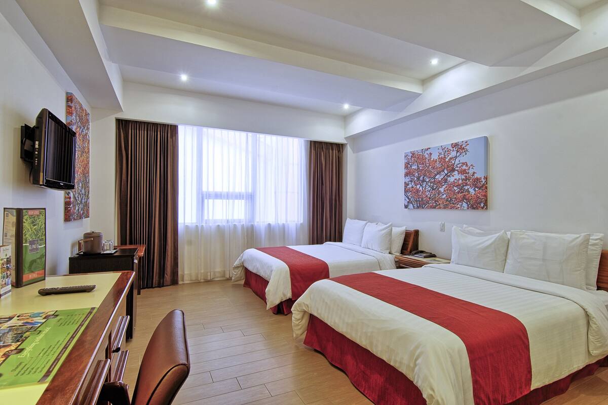 A hotel room with two beds, a desk with a chair, a TV, and a painting on the wall.