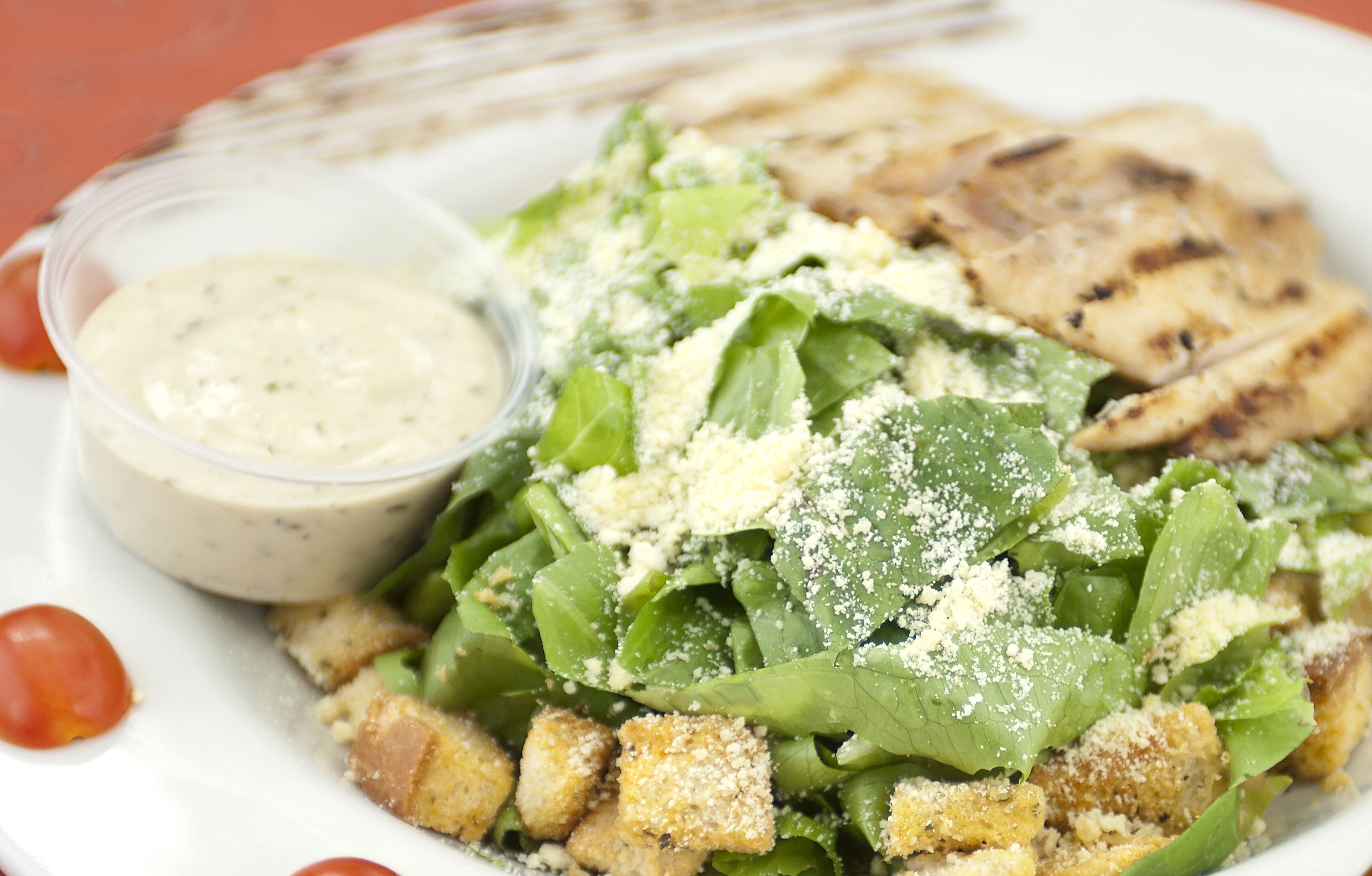 A plate of food with a salad, croutons, and grilled chicken, accompanied by a small container of dressing.
