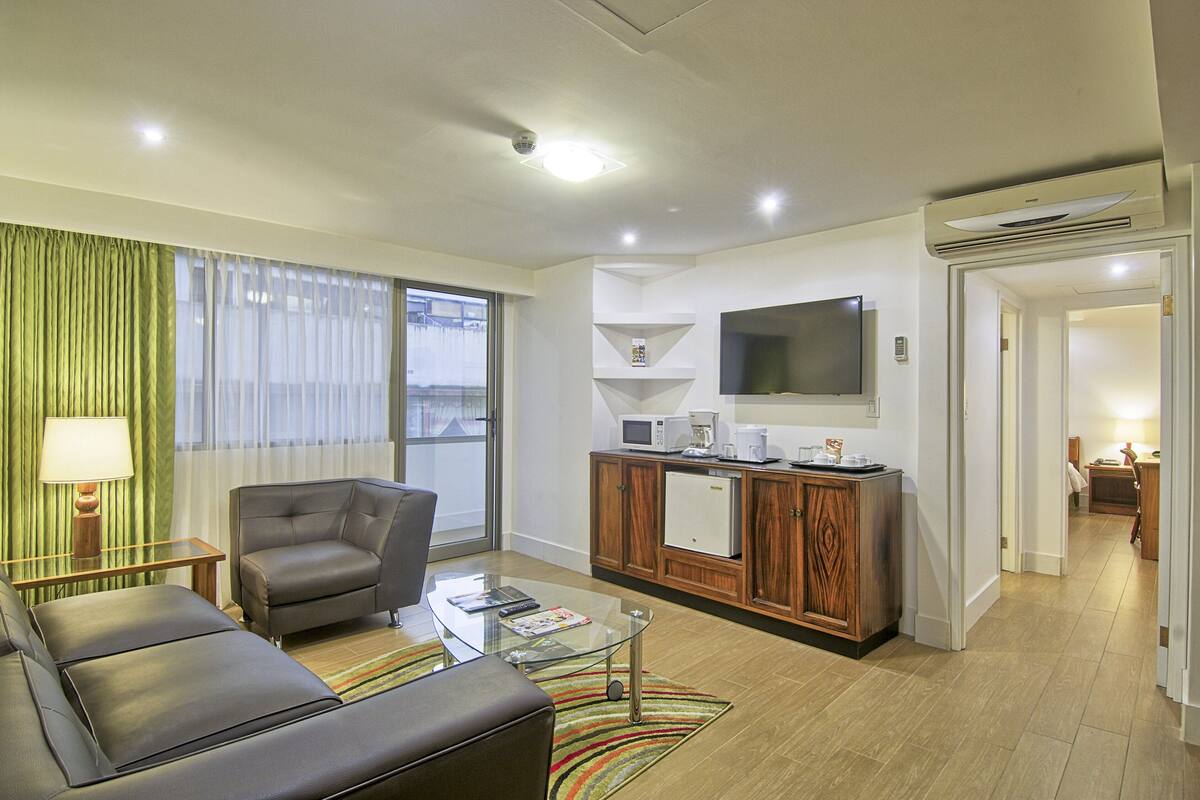 A modern living room with a leather sofa, a glass coffee table, and a television mounted on the wall.