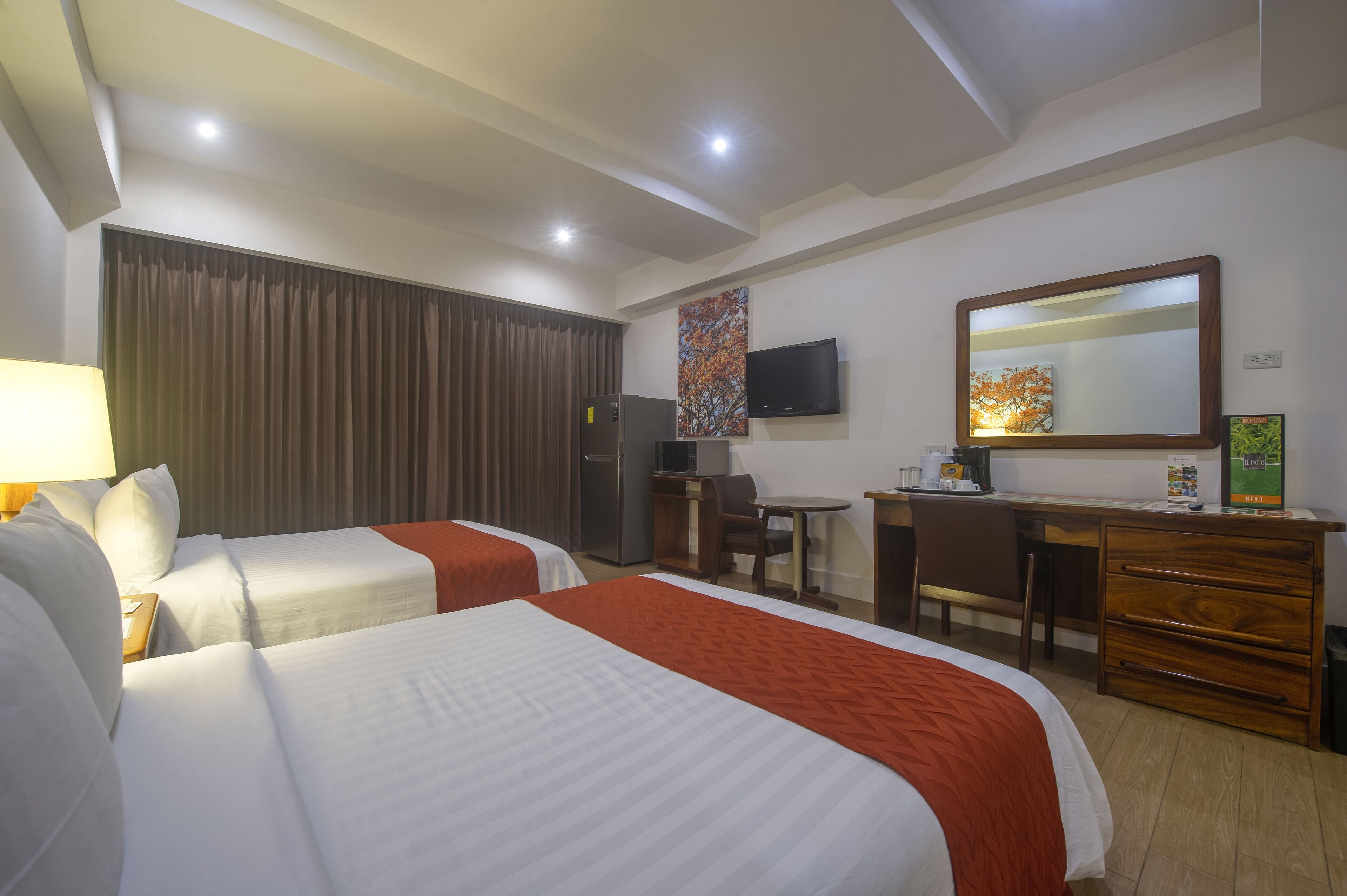 A hotel room with two beds, a desk, a chair, a television, and a mirror.