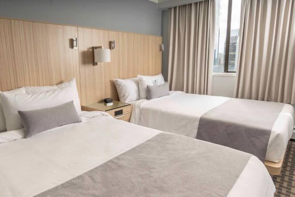 A hotel room with two beds, a wooden headboard, a nightstand, and a window with curtains.