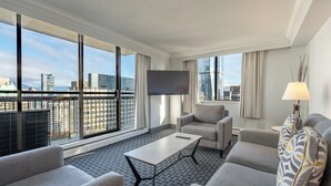 Una habitación de hotel moderna con un ventanal grande, un televisor de pantalla plana, un sofá, una mesa de centro y una lámpara.