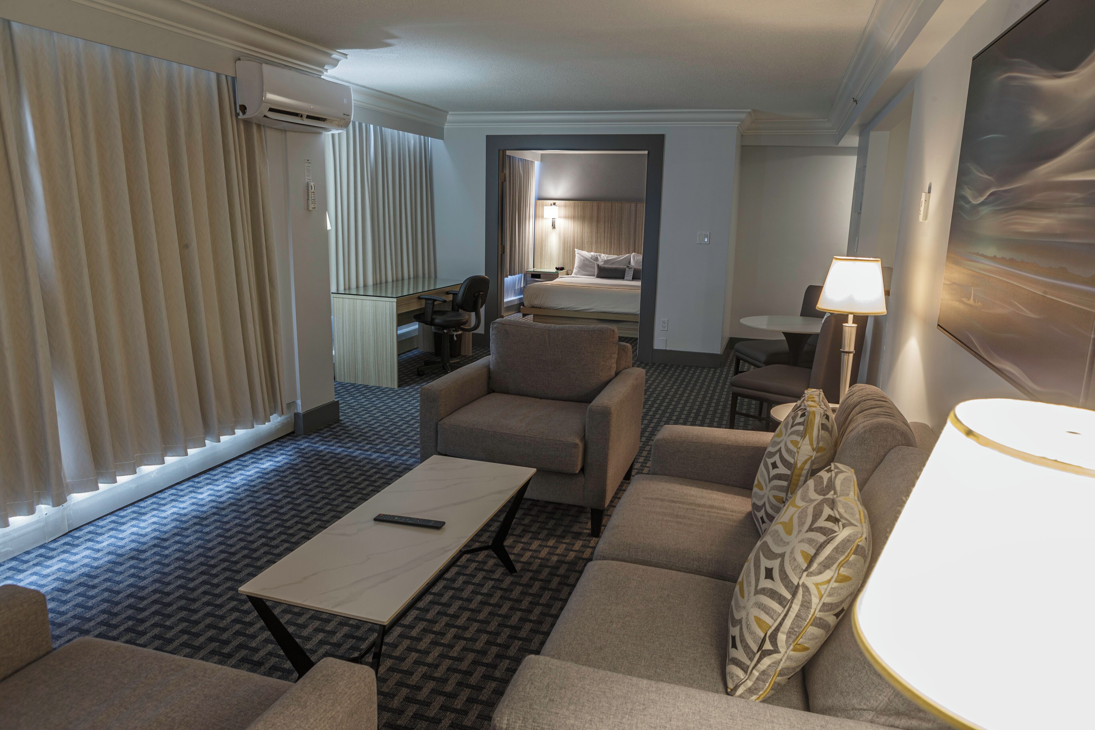 Una habitación de hotel con cama, escritorio, silla, sofá, mesa de centro y lámpara.