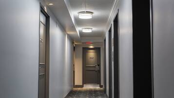 Um corredor de hotel com carpete estampado, uma porta com número e um sinal de saída vermelho.