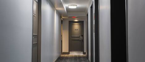 A hotel hallway with a patterned carpet, a door with a number, and a red exit sign.