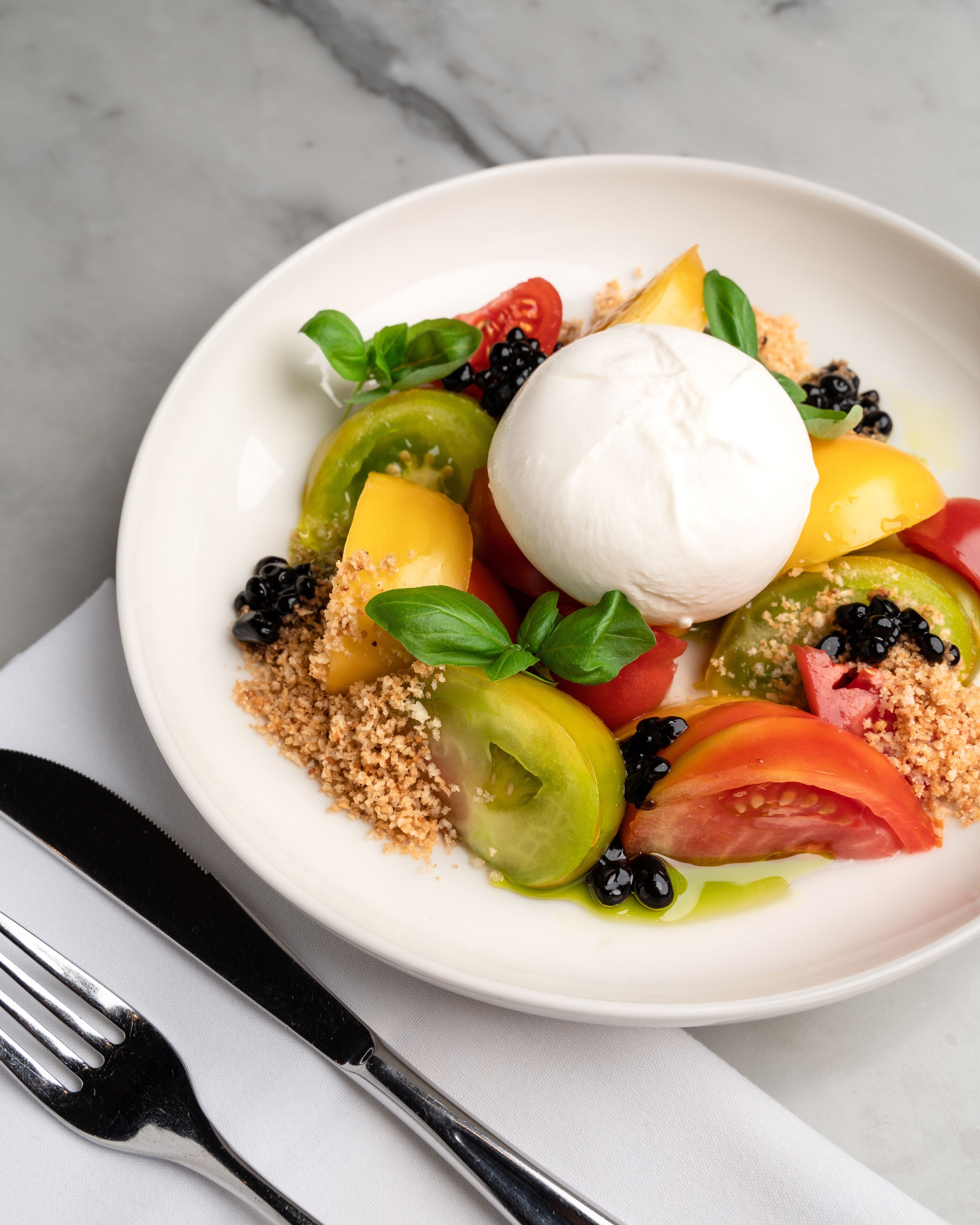 Ein weißer Teller mit einer Portion weißer Creme, Brombeeren und geschnittenem Obst auf einer Marmorplatte.