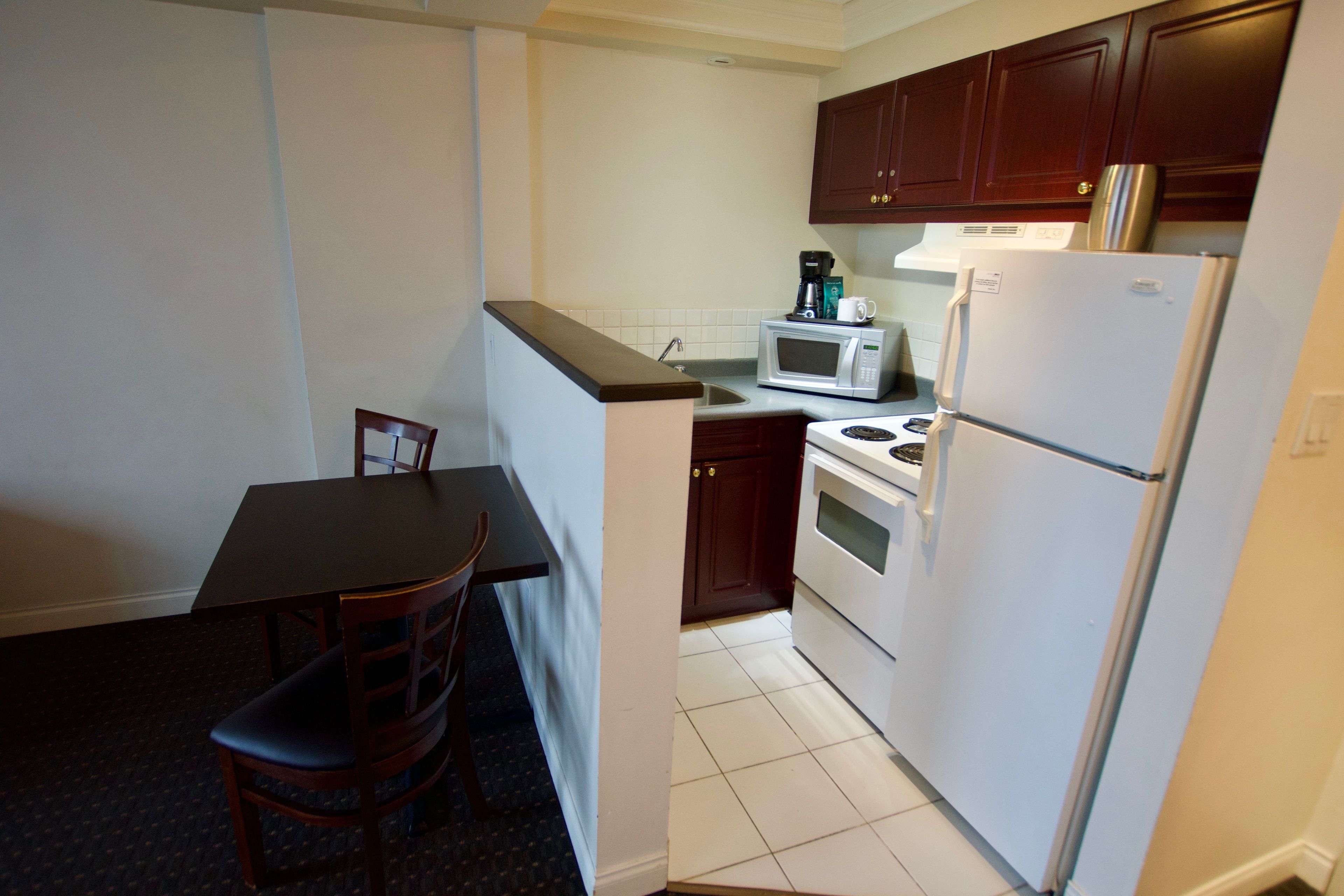 A compact kitchen with a dining table, chairs, a microwave, a stove, and a refrigerator.