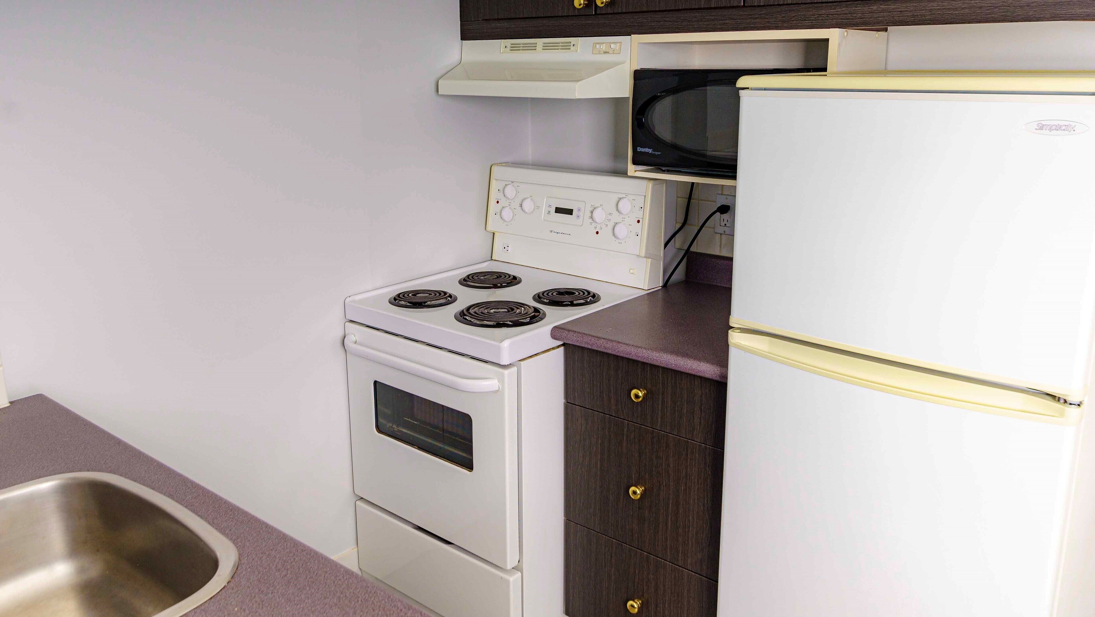 A compact kitchen with a white stove, a microwave, and a refrigerator.