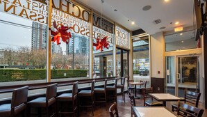 Un comedor interior con asientos tipo cabina y mesas, ventanas amplias con lazos decorativos y vistas al paisaje urbano.