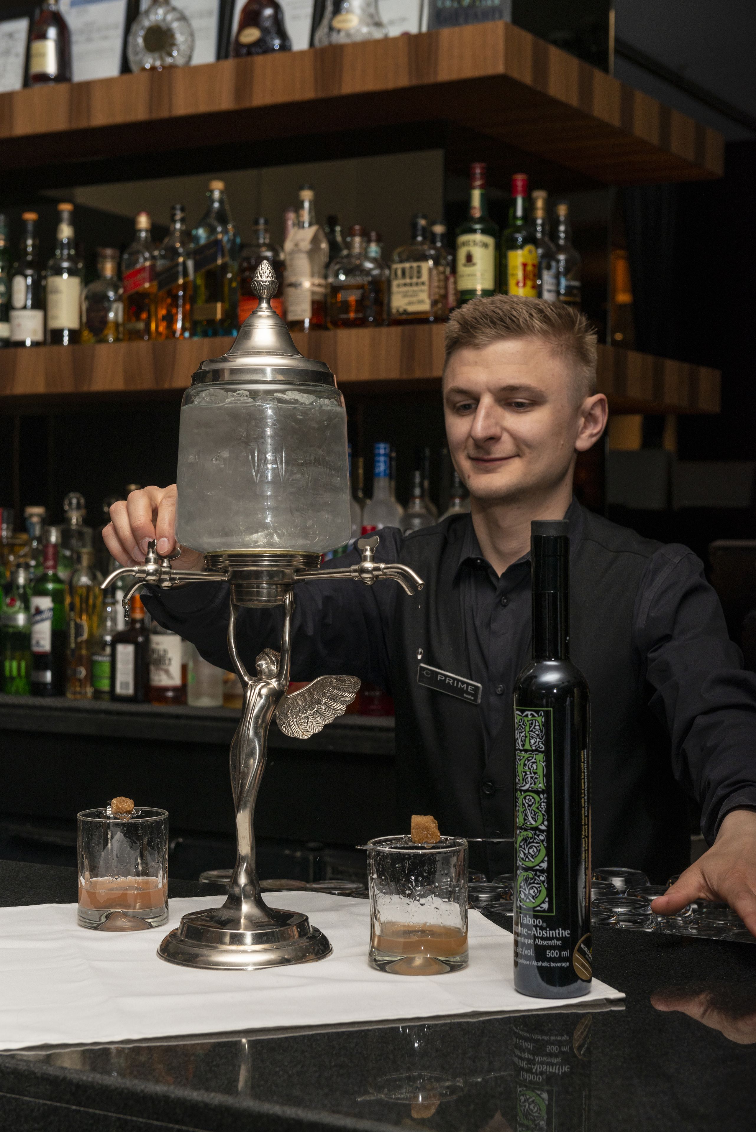 Un bar con un cantinero preparando bebidas, un dispensador de hielo grande y varias botellas de licor en estantes.