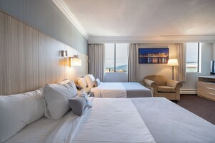 Habitación de hotel con dos camas, una silla, un escritorio y un amplio ventanal con vistas a la ciudad.