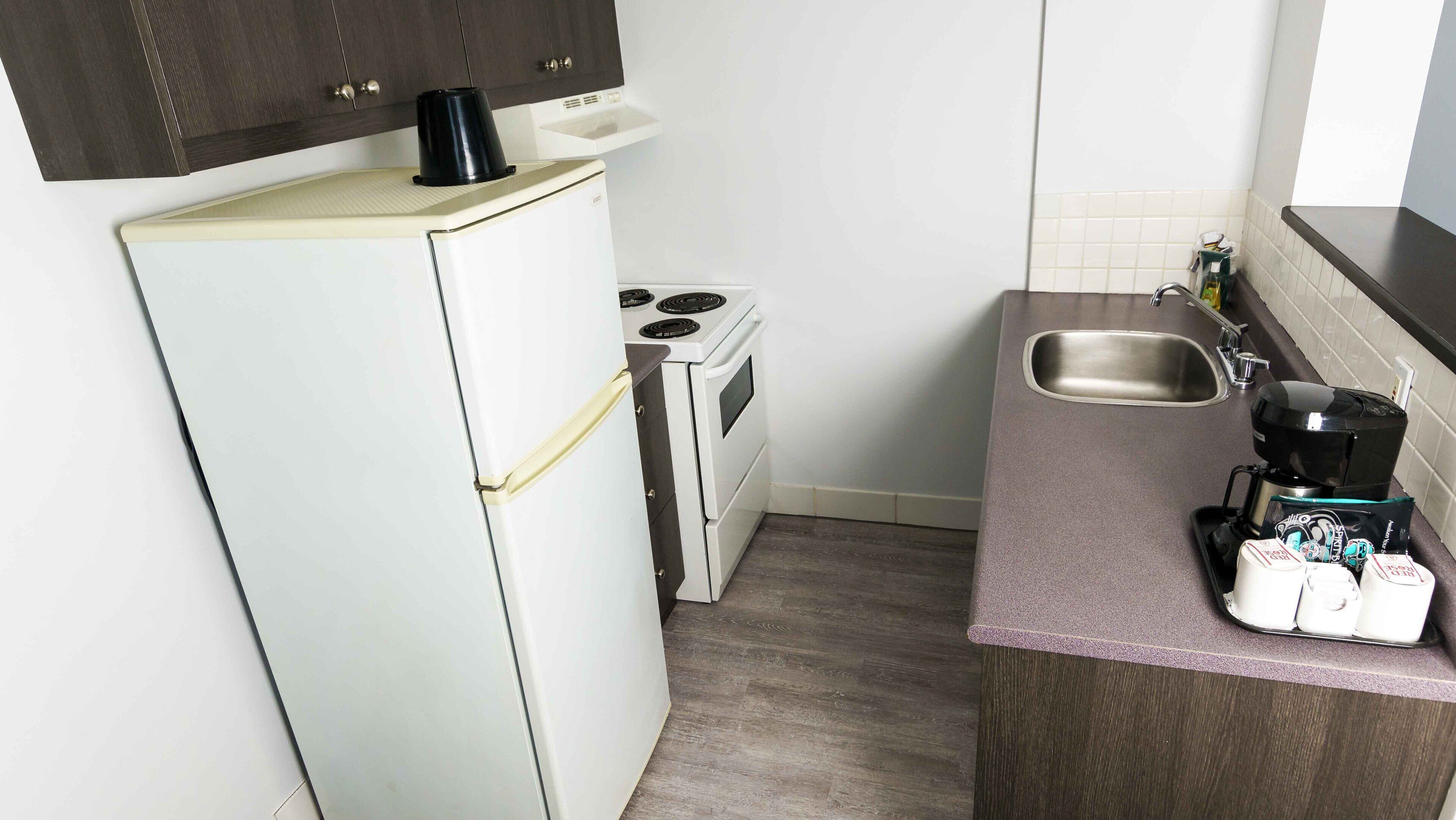 A compact kitchen with a refrigerator, stove, sink, and coffee maker.