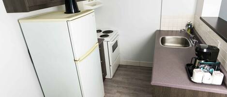 A compact kitchen with a refrigerator, stove, sink, and coffee maker.