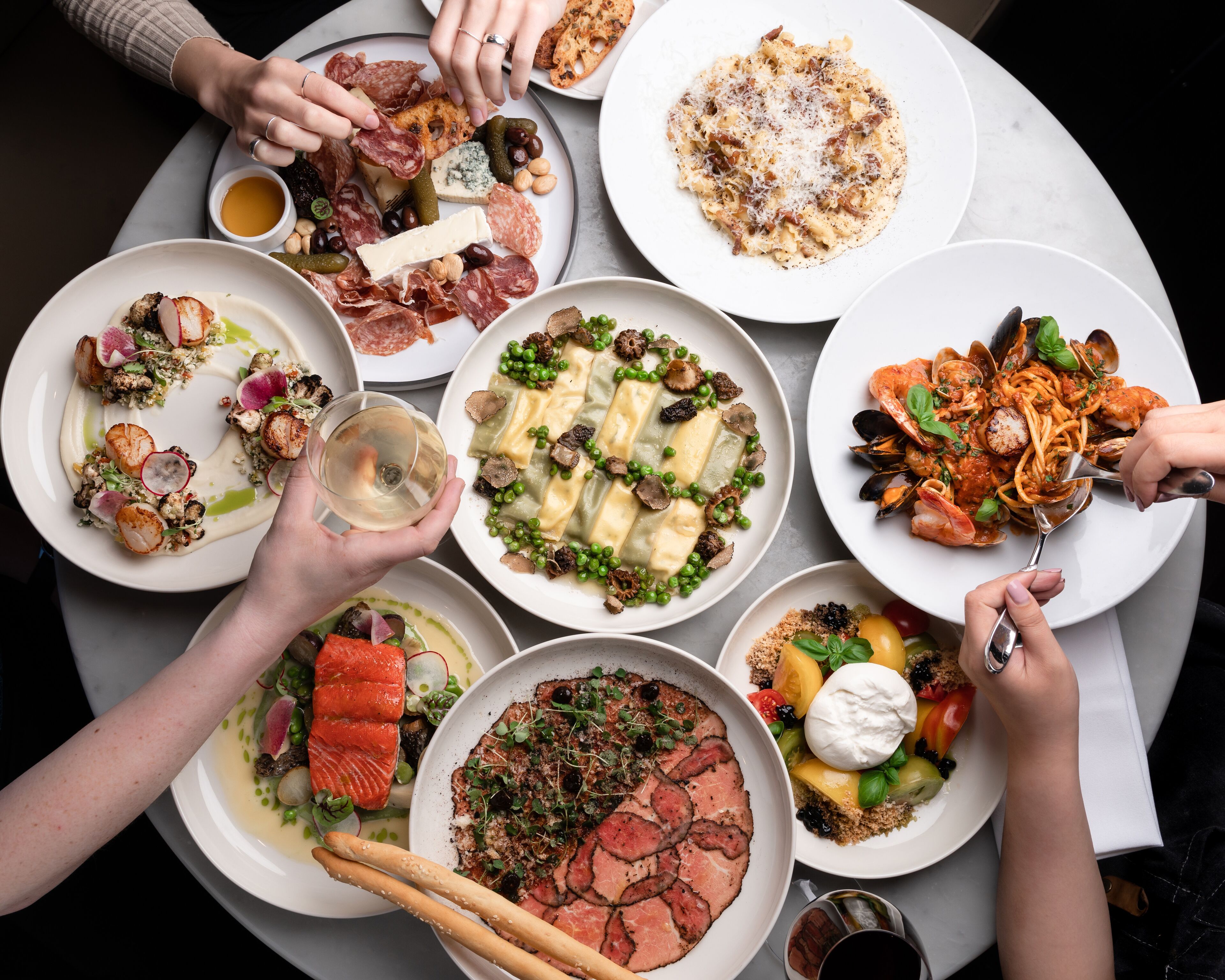 Una mesa con diversos platos, entre ellos mariscos, pasta y carnes, que sugiere un ambiente para comer.