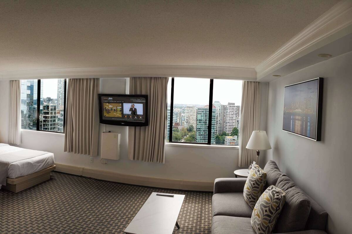 A hotel room with two beds, a sofa, a TV, and a city view.