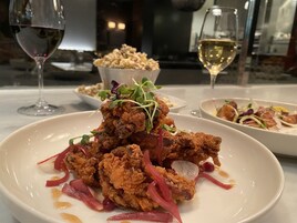 Una mesa de comedor con un plato de pollo frito, un cuenco de palomitas de maíz y dos copas de vino blanco.