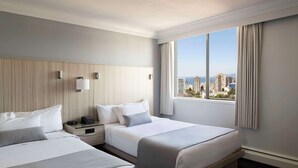 Habitación de hotel con dos camas, un ventanal grande con vista a la ciudad y un diseño moderno.