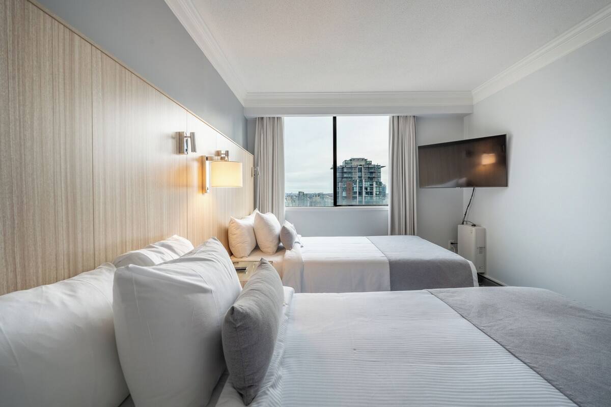A hotel room with two beds, a TV, and a city view.
