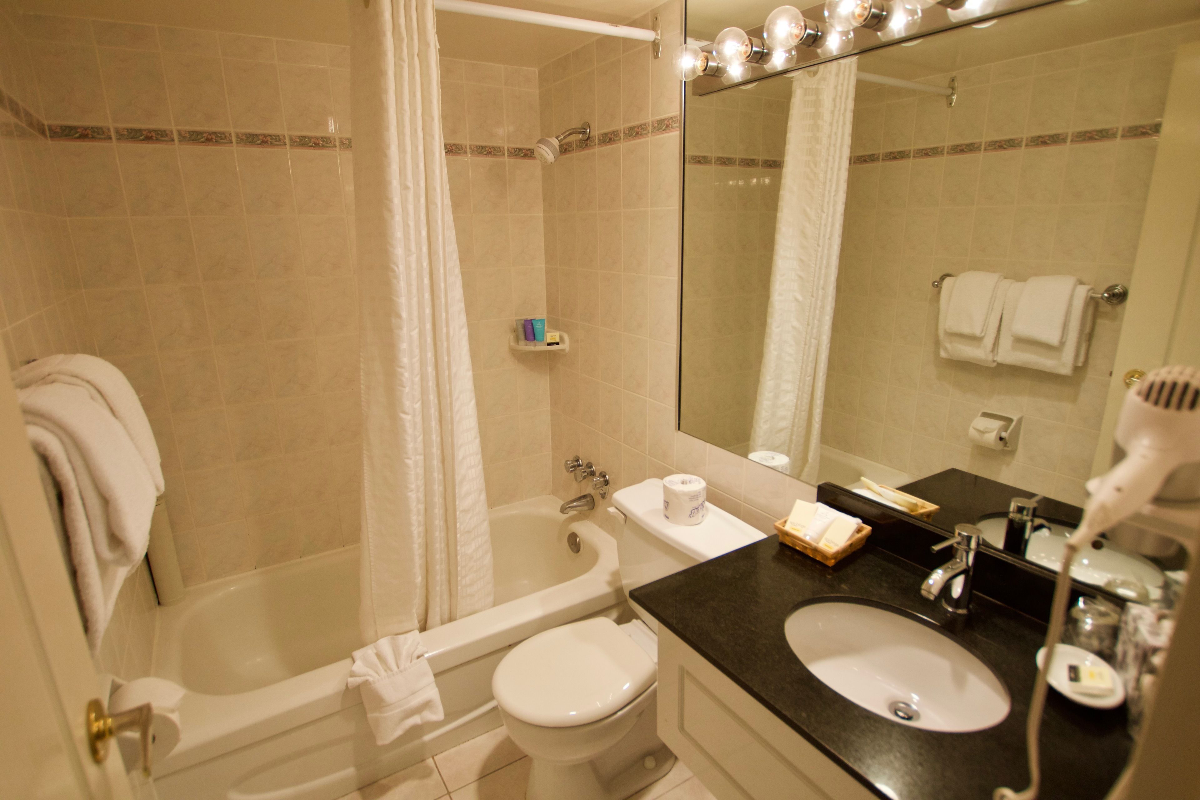 A bathroom with a bathtub, toilet, sink, and a mirror with lights.
