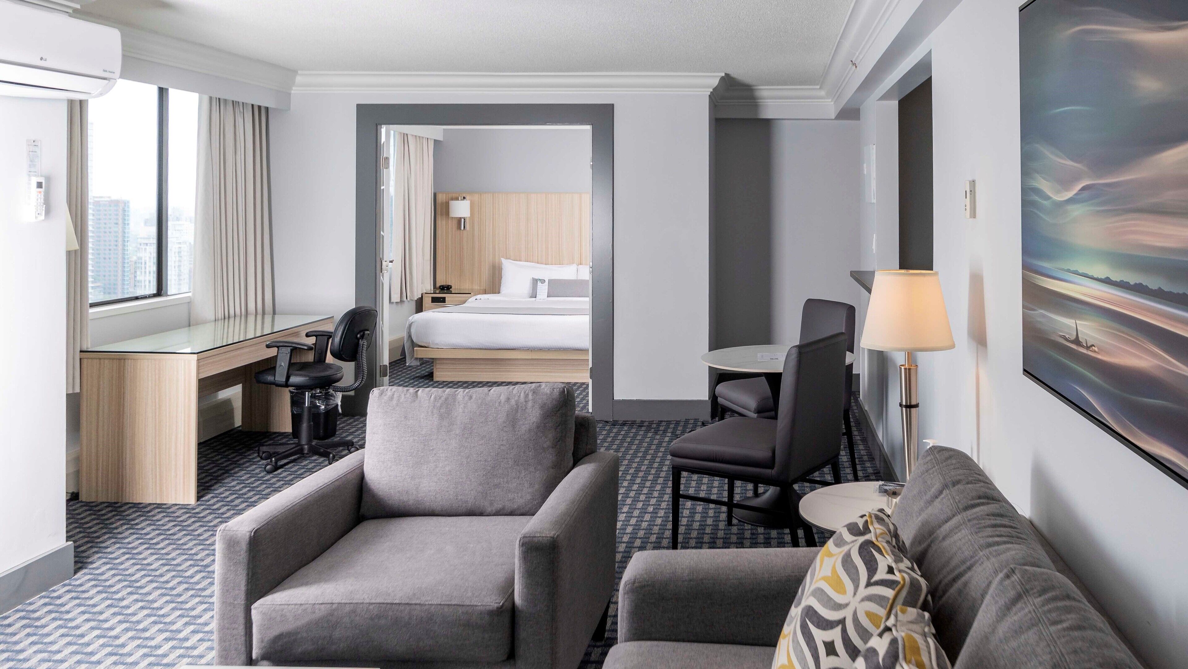 A hotel room with a bed, desk, two armchairs, a small table, and a lamp.