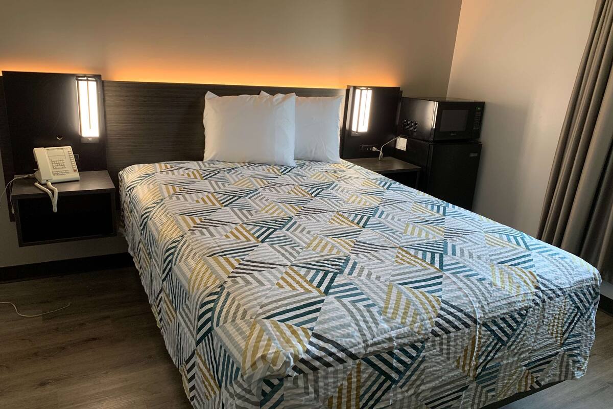 A hotel room with a large bed, two bedside tables, a nightstand with a telephone, and a TV on a stand.