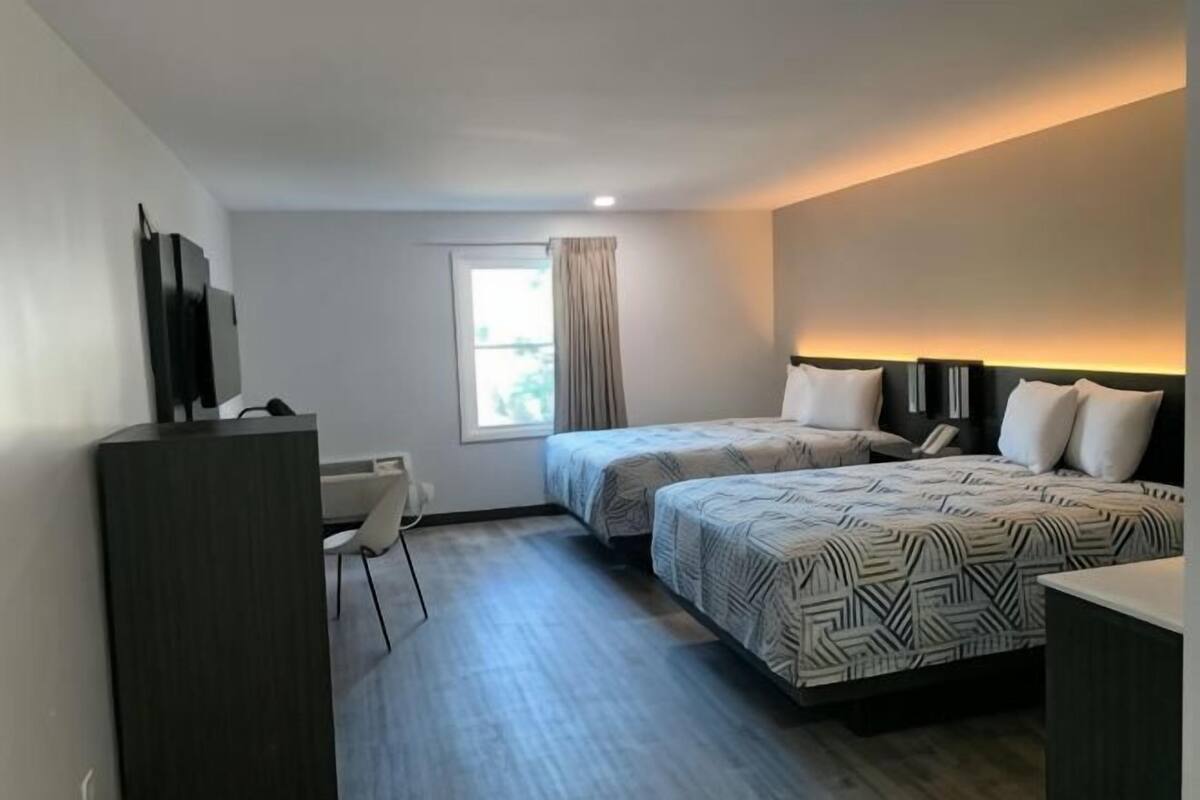 A hotel room with two beds, a desk, a chair, a TV, and a window with curtains.