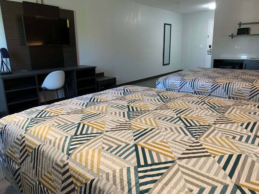 A hotel room with a large bed, a desk, a chair, a TV, and a mirror.