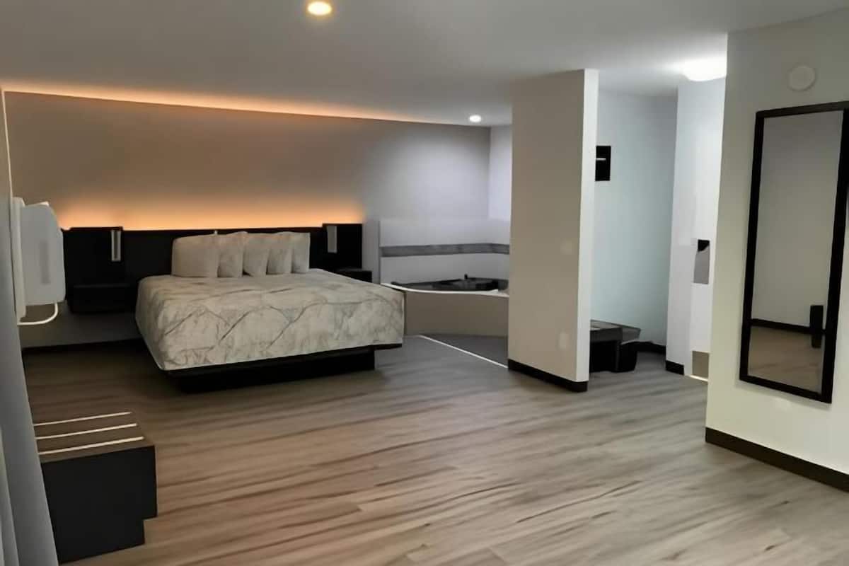A modern hotel room with a large bed, a small desk, a chair, a mirror, and a walk-in closet.
