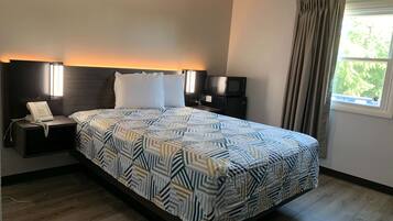 Quarto de hotel com uma cama grande, mesas de cabeceira, telefone, micro-ondas e janela com cortinas.