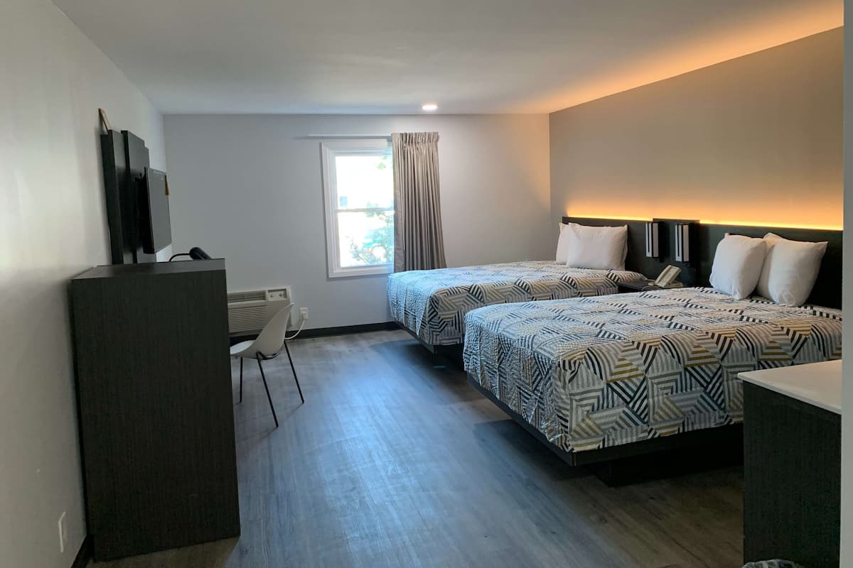 A hotel room with two beds, a desk, a chair, a TV, and a window with curtains.