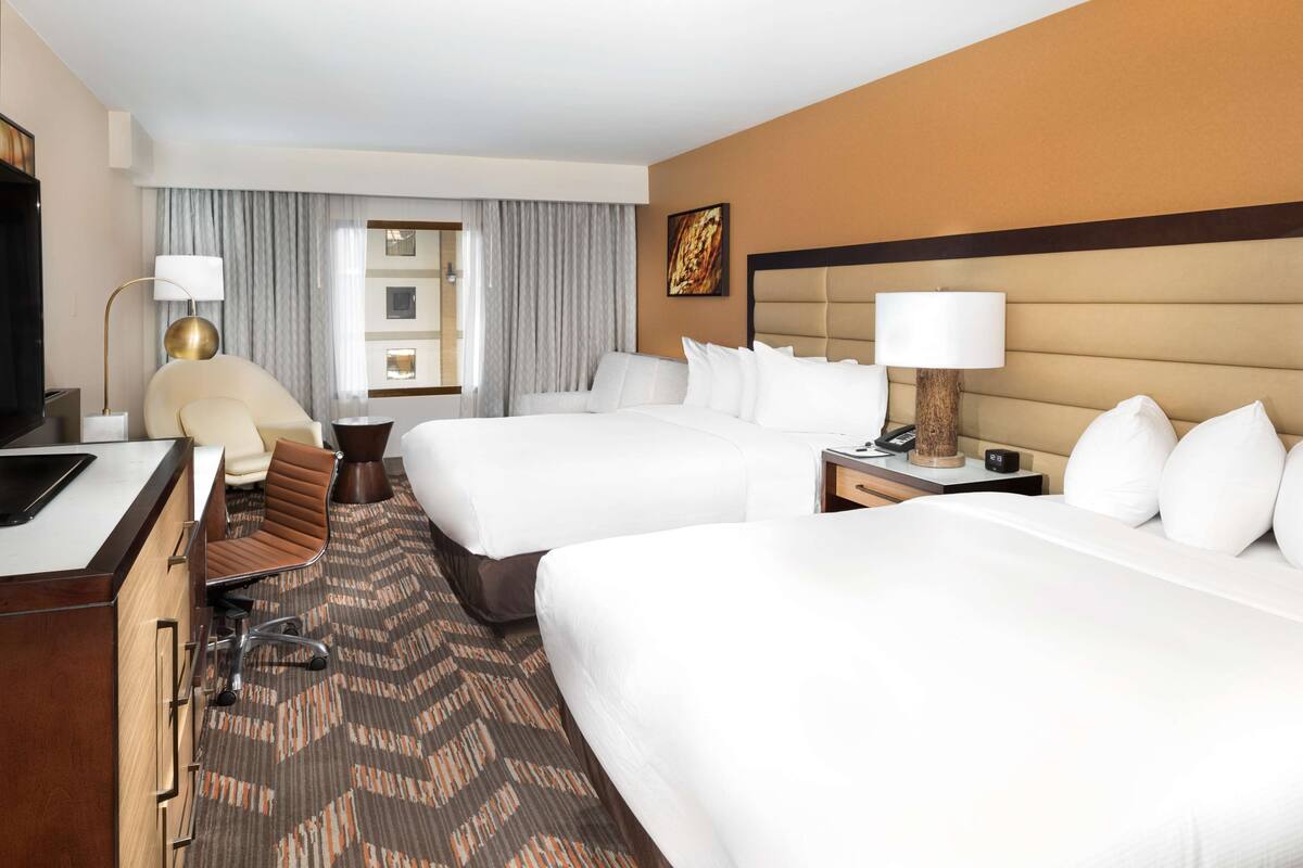 A hotel room with two beds, a desk, a chair, a lamp, and a carpeted floor.