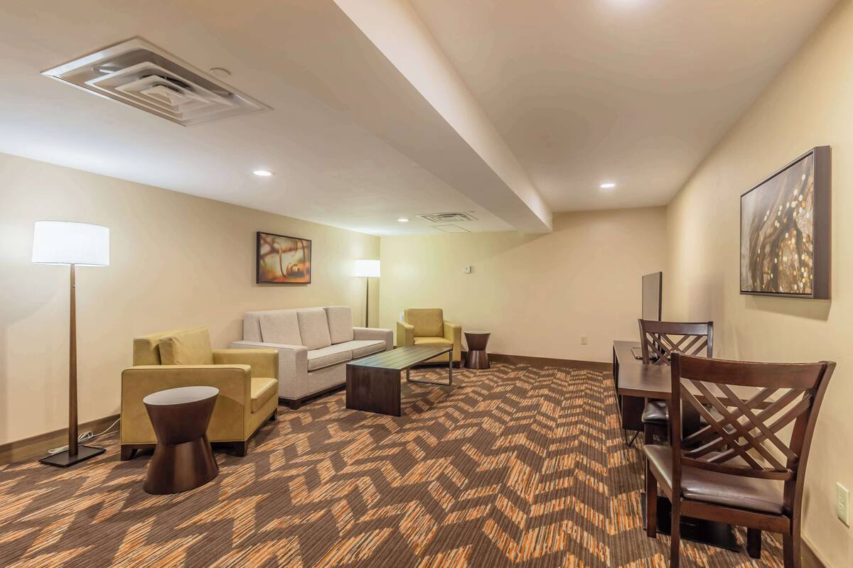 A hotel room with a sofa, armchairs, a coffee table, a dining table with chairs, a lamp, and artwork on the walls.