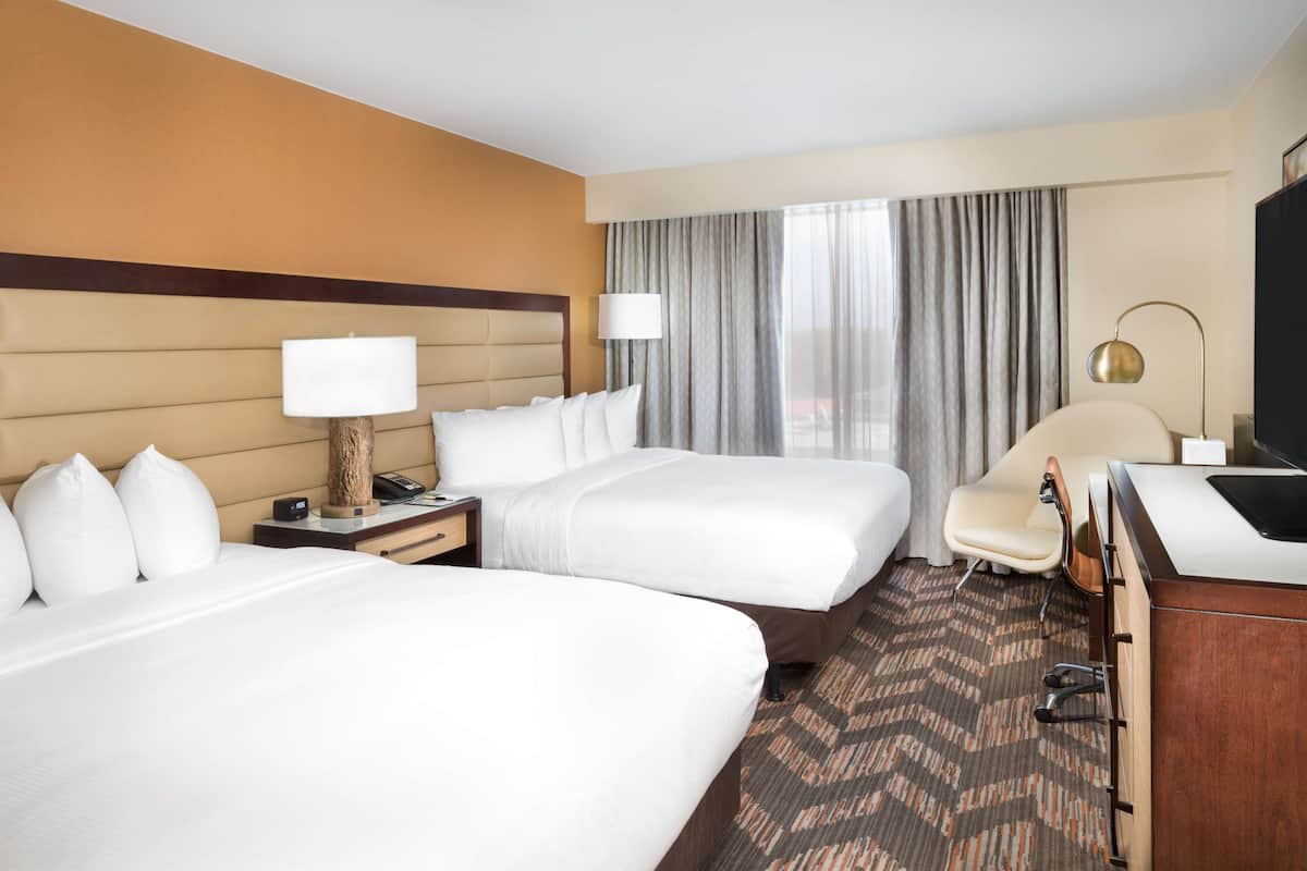 A hotel room with two beds, a desk, a chair, a TV, and a window with curtains.