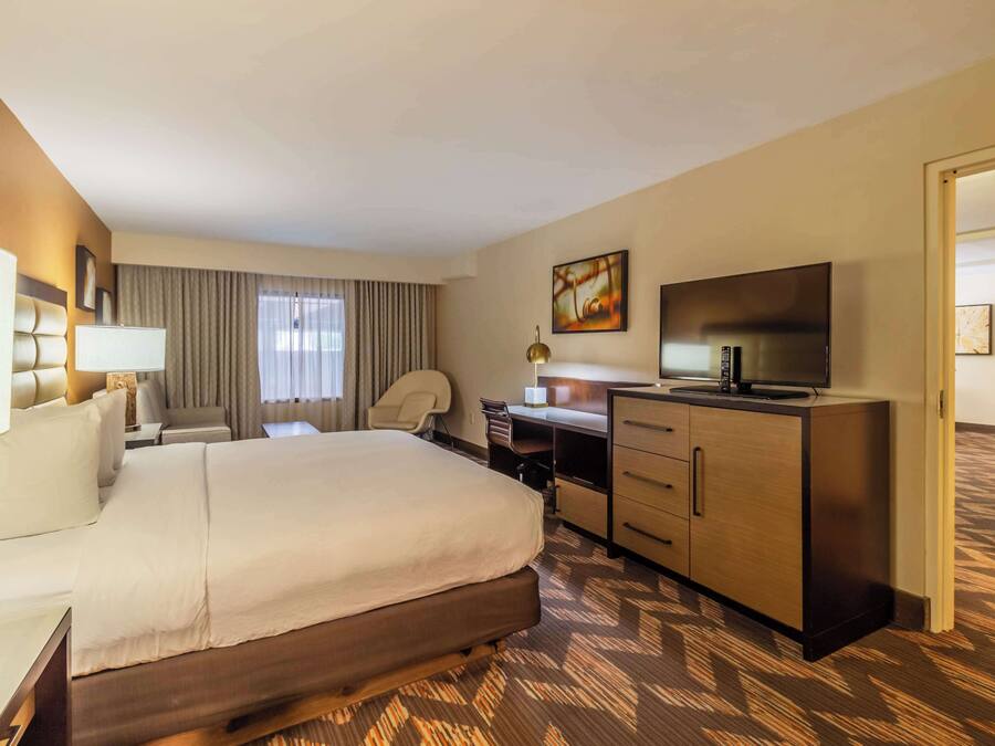 Una habitación de hotel con una cama grande, un escritorio con silla, un televisor y un armario.