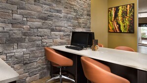 Un espacio de oficina moderno con pared de piedra, una computadora de escritorio, dos sillones de cuero y un cuadro enmarcado en la pared.