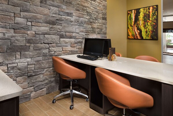Un espacio de oficina moderno con pared de piedra, una computadora de escritorio, dos sillones de cuero y un cuadro enmarcado en la pared.