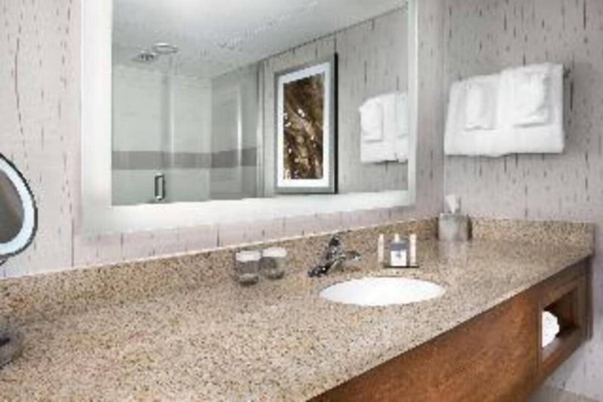 A bathroom with a granite countertop, a sink, a mirror, and a shower.