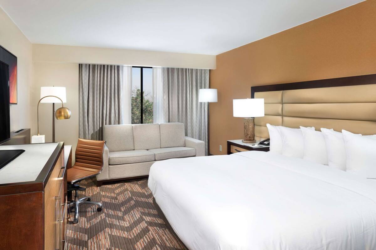 A hotel room with a bed, a sofa, a desk, and a TV.