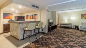 Un hall de hotel con una recepción, dos sillones, un televisor, un sofá y una alfombra estampada.