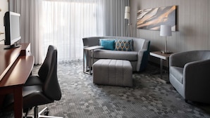 A hotel room with a grey sofa, a grey armchair, a wooden desk with a computer, and a lamp. - Sonesta Select Phoenix Camelback (Phoenix)