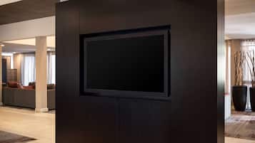 En modern entréhall med en stor, platt-TV som är monterad på en mörk träpanel, en sittgrupp med soffor och stora krukväxter.