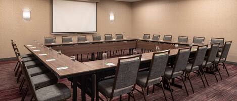 A conference room with a long table, chairs, a projector screen, and a carpeted floor.