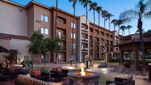 A courtyard with outdoor seating, a fire pit, and a multi-story building with balconies and palm trees. - Sonesta Select Phoenix Camelback (Phoenix)