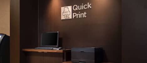 Un mostrador de recepción con una computadora portátil y una impresora, un letrero en la pared que dice "Quick Print" y un diseño de panel de madera.