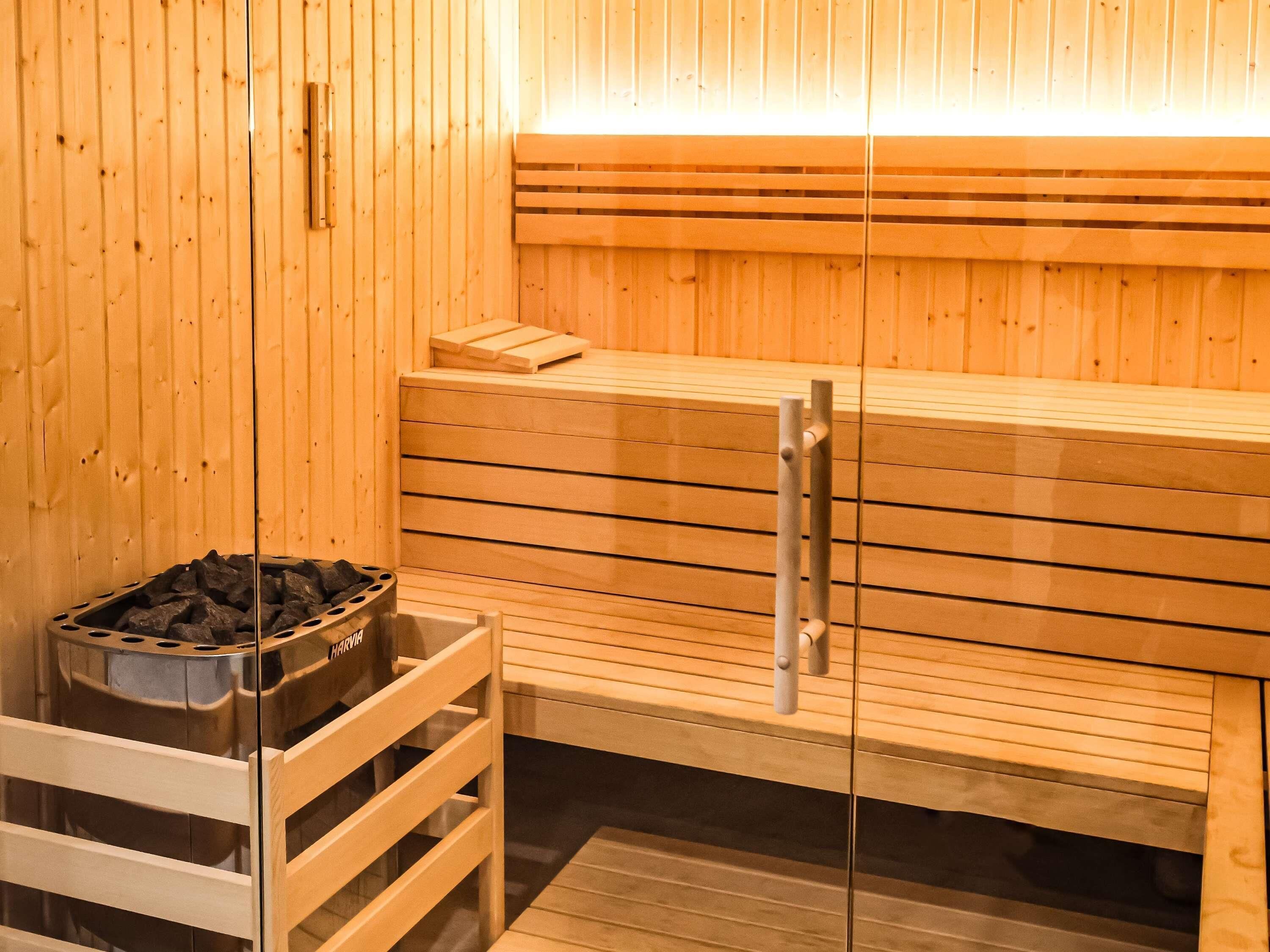 A sauna with wooden benches and a glass door, a metal container with charcoal, and a wooden bench with a towel.