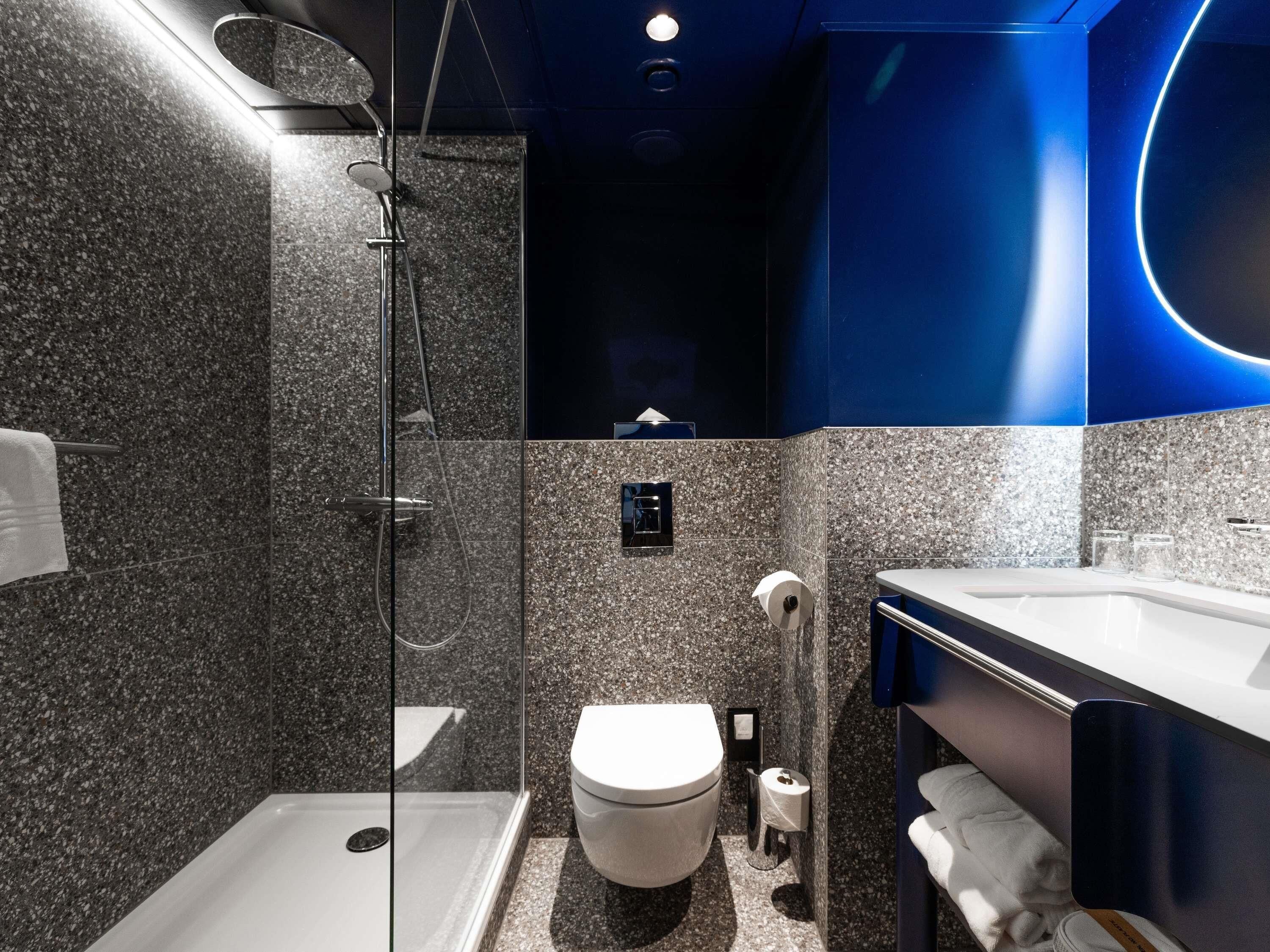 A modern bathroom with a glass-enclosed shower, a toilet, and a sink with a mirror.