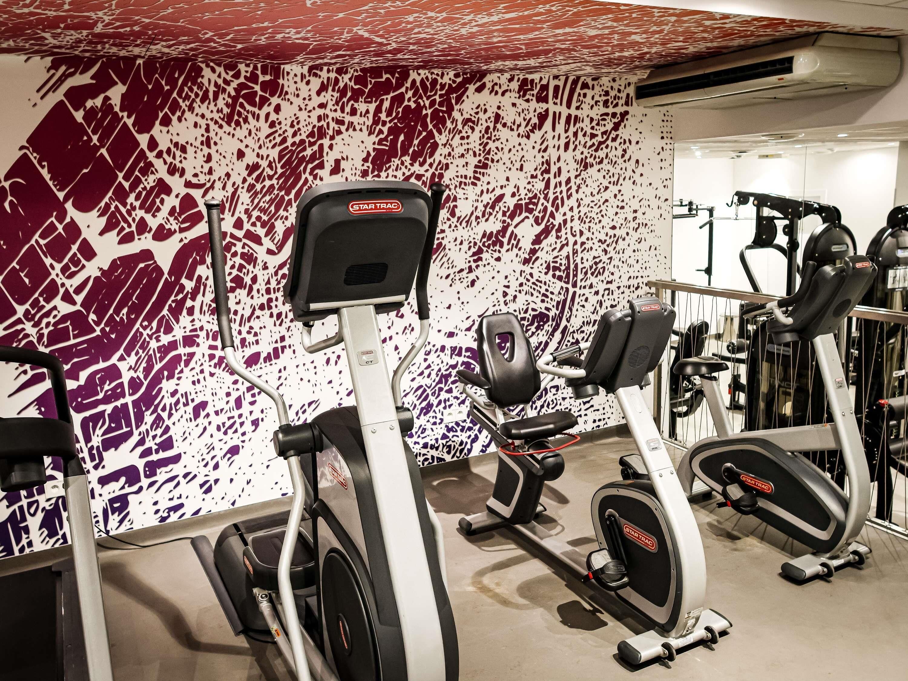 A gym with stationary bikes and ellipticals, a red and white patterned wall, and a mirror reflecting the equipment.