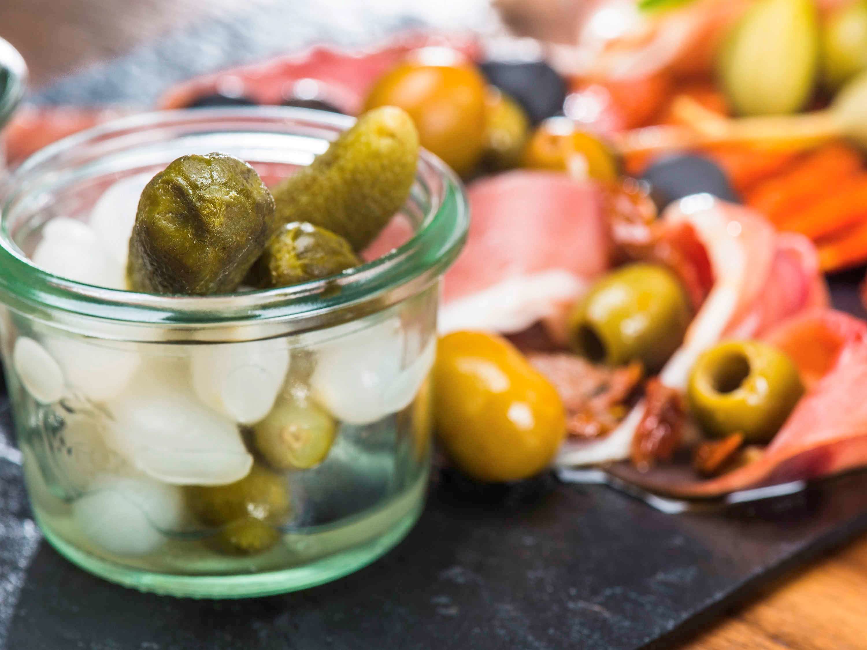Un tarro de vidrio lleno de aceitunas y pepinillos sobre una tabla de pizarra negra.